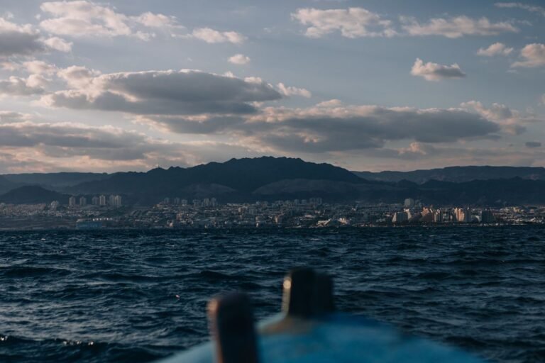 A picturesque view of Aqaba cityscape with mountains, sea, and a passing boat at twilight.