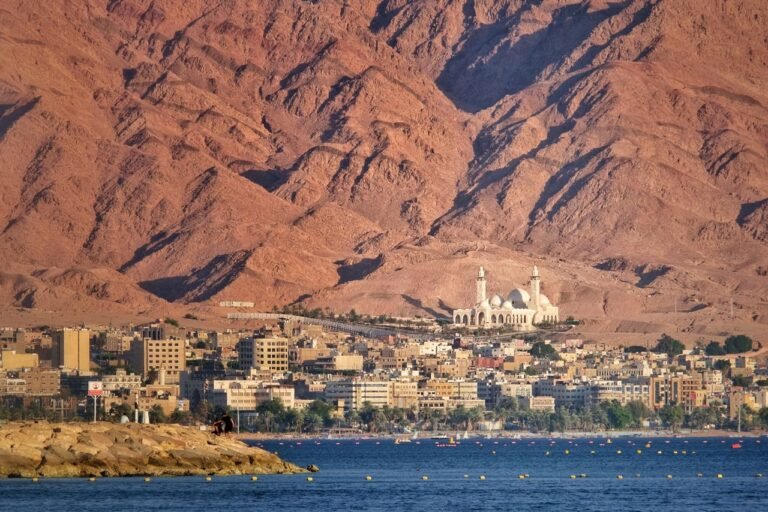 4 Days Petra & Wadi rum & Aqaba & Dead sea A scenic view of Aqaba city against a dramatic mountain backdrop by the sea.